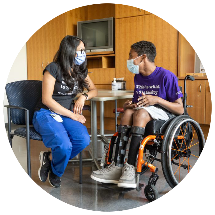An adult on the left and a teenager sitting on wheelchair on the right