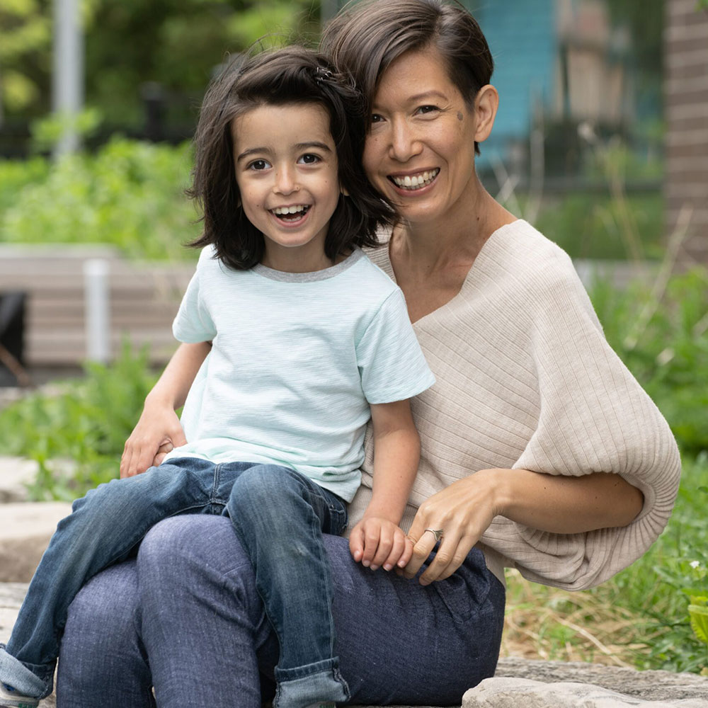 A young boy wearing a whit t-shirt and blue jeans sitting on his mom's lap. She's wearing a knit top and blue jeans.