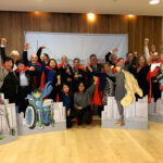 A group of employees gather in front of a Capes for Kids banner as part of a team building activity.