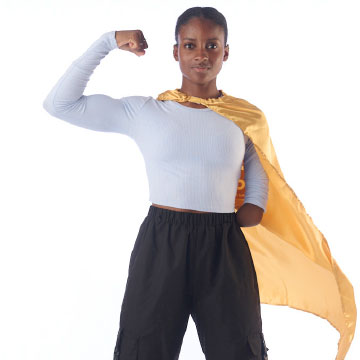 Teen in white top and black pants wearing a cape. She's holding up an arm in a superhero pose