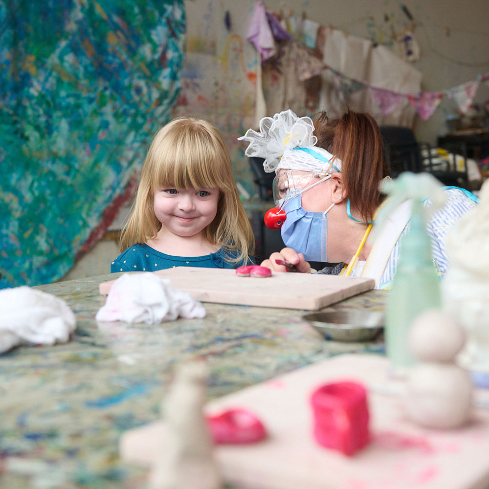 A young girl and an adult with a red clown nose in an art studio