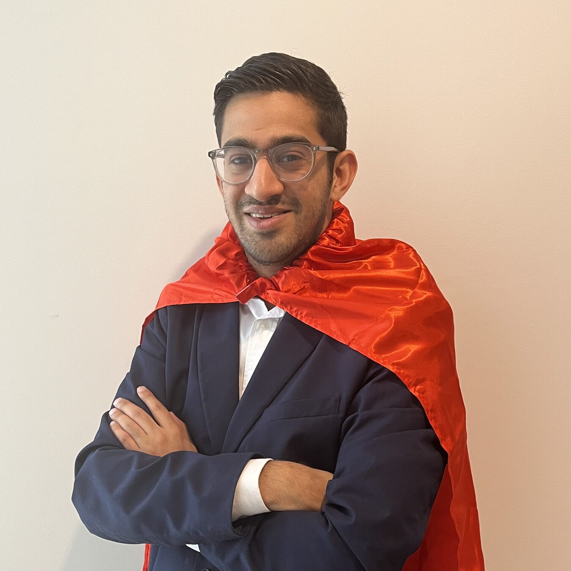 Smiling person with short hair and glasses wearing a red cape and black blazer.