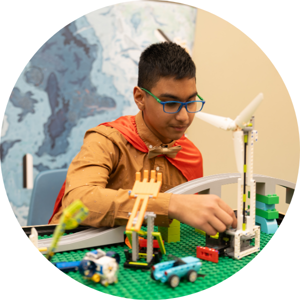 A young boy wears a red cape and plays with LEGO