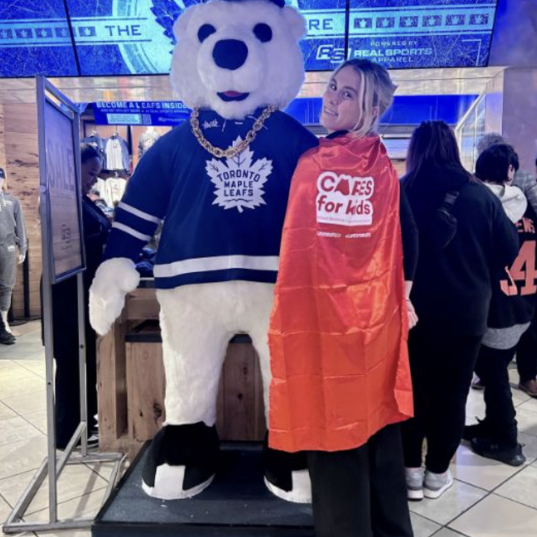 An adult wearing a red cape taking a photo with Carlton the Bear